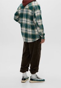 Camicia flanella a quadri in verde, bianco e nero; vestibilità ampia; abbinata a pantaloni in corduroy marrone scuro e sneakers chunky con dettagli grigi.