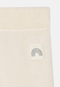 Tissu couleur crème avec une texture douce présentant une petite étiquette embossée d'un design de arc-en-ciel multicolore, cousue sur un côté.