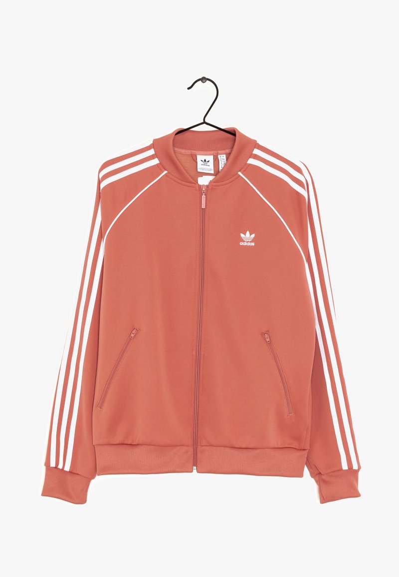 Adidas sportovní bunda v korálové barvě s bílými pruhy, plný zip vpředu, stojáček a dvě boční kapsy. Vyrobena z hladkého materiálu.
