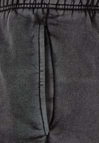 Pantaloni da felpa grigio scuro con una texture morbida, cintura elastica e tasche laterali. Il tessuto sembra leggero e liscio.