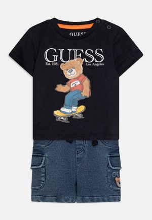 T-shirt de algodão preto com uma ilustração de um urso vestindo uma camisa vermelha e andando de skateboard, combinado com calções de ganga com bolsos cargo e um logotipo.