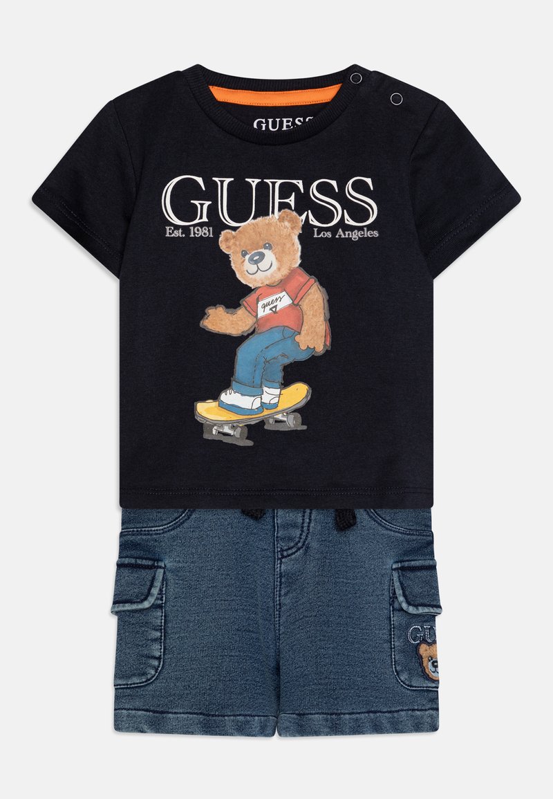 T-shirt de algodão preto com uma ilustração de um urso vestindo uma camisa vermelha e andando de skateboard, combinado com calções de ganga com bolsos cargo e um logotipo.