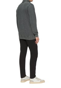 Vervaagde grijze sweatshirt met een hoge hals, gecombineerd met zwarte slim-fit broek en witte sneakers met beige accenten. Eenvoudige ontwerpelementen zichtbaar.
