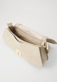 Bolsa de mão de imitação de couro bege com um acabamento texturizado, apresentando um fecho em tom de ouro e um bolso interior com zíper. Inclui uma alça ajustável.