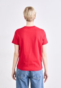 Rode katoenen t-shirt met korte mouwen en een ronde halslijn, gecombineerd met lichtblauwe spijkerbroek. Eenvoudig ontwerp en een relaxte pasvorm.