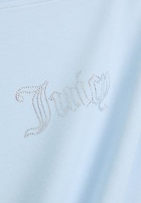 Ανοιχτό μπλε βαμβακερό μπλουζάκι με διακοσμητικά μέταλλα από ασημί κρυσταλλίδες σε σχέδιο σ spiraling γραμματοσειράς στο μπροστινό μέρος. Λείο υφή.