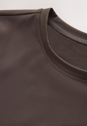 Braunes Sportshirt mit glatter Textur, Rundhalsausschnitt und dezenten Nahtdetails. Fokus auf Stoffzusammensetzung und Design.