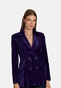 Blazer doppiopetto in velluto viola con revers a punta, texture verticale, doppie tasche e dettagli in bottoni dorati.