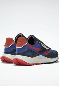 Sneakers med en svart textilövre del, blå och röda accenter, en mocka hälschaufför och en vit sula med röda detaljer och strukturerat grepp.