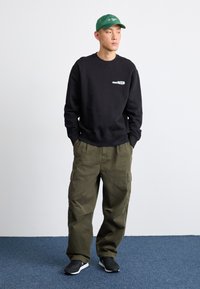 Sweatshirt negru cu logo, pantaloni cargo oliv, șapcă verde și adidași negri. O ținută casual cu o siluetă relaxată. Bumbac texturat și țesătură durabilă.