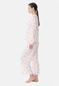 Lightweight, cream-colored pajama set featuring a print of small pink kiss marks. Long sleeves, loose-fitting pants with wide leg design.