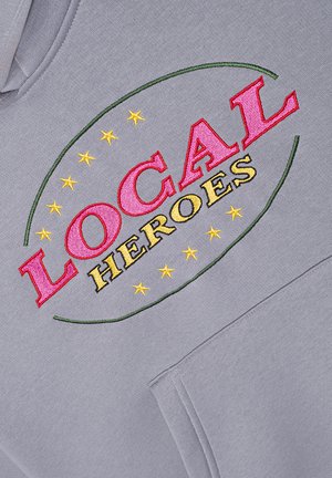 Szara bluza z haftowanym napisem "LOCAL" na czerwono i "HEROES" na żółto, otoczona zielonym owalem z żółtymi gwiazdami. Zawiera kieszeń typu kangurka.