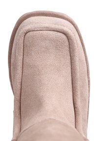 Stivale alla caviglia in suede beige con punta tonda e dettagli di cucitura. Texture morbida e design a strati. Suola visibile e bordi lisci.