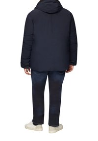 Marineblauer Pufferjacke mit Kapuze, die eine glatte Textur und ein einfaches Design aufweist. Kombiniert mit dunkelblauen Jeans und weißen Sneakers.