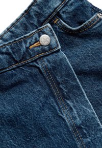 Jeans de mezclilla de tono azul oscuro, con costuras de cobre, cierre de botón y sutiles detalles de textura. Presenta un bolsillo delantero en el lado derecho.
