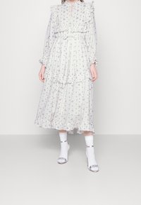 Vaalea kukkakuosis maxi-mekko, jossa on rypytetty kaula-aukko ja hihat, pleatattu pinta ja kerrostetut kerrokset. Yhdistetty valkoisten sukkien ja hopeisten korkokenkien kanssa.