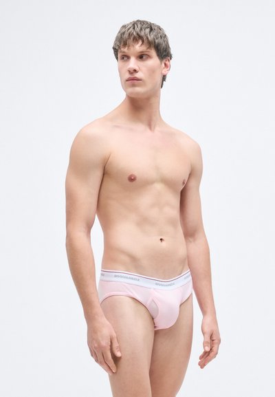 Ροζ βαμβακερό σλιπ με υφή, ελαστική ζώνη μέσης με λογότυπο και κλασικό σχέδιο σλιπ. Το μοντέλο ποζάρει με ουδέτερη έκφραση.