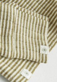 Gestreepte stof in olijfgroen en roomkleur, met een zachte textuur en kleine zonlogo-labels op de hoeken. Verticale strepen zijn overal zichtbaar.