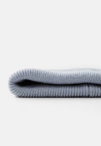 Tessuto lavorato a maglia azzurro chiaro piegato ordinatamente, che mostra una texture a coste e bordi lisci, enfatizzando il materiale morbido e caldo.