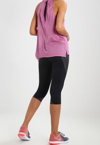 Top deportivo rosa sin mangas con espalda en forma de llave, combinado con mallas capri negras con detalles de malla y zapatillas deportivas grises con rojo.