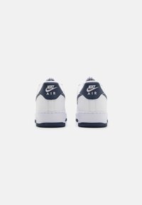 Bijele Nike Air tenisice s tamnoplavi naglascima, s glatkom kožnom gornjom površinom, gumenenim potplatom i detaljem s brandom na peti. Klasični nisku-top dizajn.