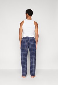 Marineblå rutete pysjamasbukser med løs passform, featuring justerbar midje og en myk tekstur, sammen med en hvit tank top.