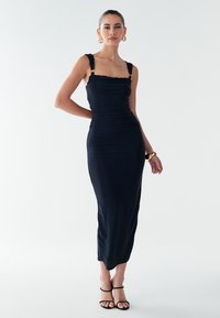 Juoda aptempianti suknelė su surinktąja tekstūra, plačiomis petnešėlėmis ir iki vidurio blauzdos ilgiu. Petnešėlėse auksinės detalės. Minkšta, tampri medžiaga.