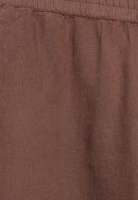 Tissu marron avec une taille élastique froncée, montrant la texture et les détails de couture fines sur la couture de la taille.