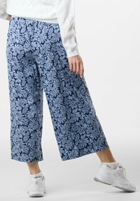 Blå blommig tryck vid byxor med elastisk midjeband och sidfickor, tillverkade av lätt material. Matchas med vita sneakers.