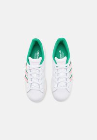 Vita sneakers med grön kant, rosa ränder, texturerat material på tån och sn ören. Har framträdande varumärke på tungan och innersulan.