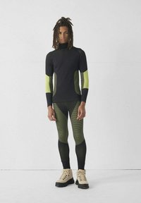 Abbigliamento sportivo aderente in nero e giallo neon. Maniche lunghe con dettagli a righe, abbinate a leggings coordinati. Tessuto strutturato.