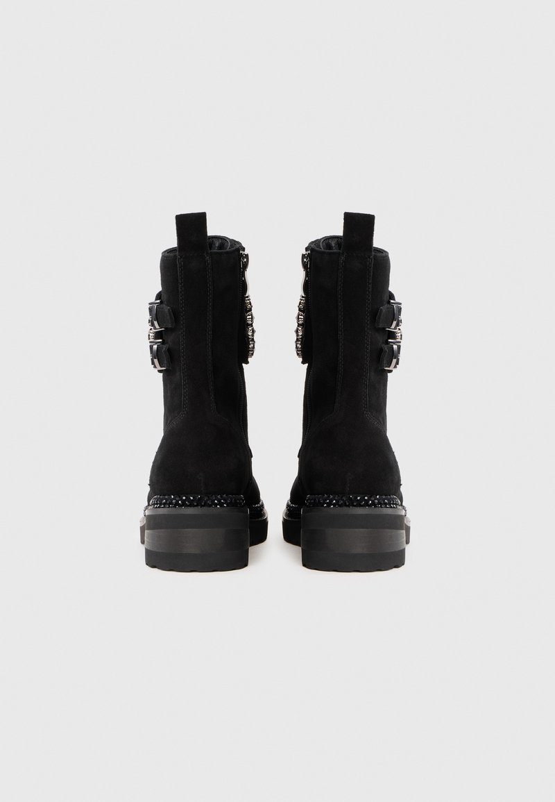 Bottes de cheville en daim noir avec quincaillerie en argent décorative, semelle épaisse noire et fermeture éclair sur le côté. Fini propre et texturé avec des languettes arrière.