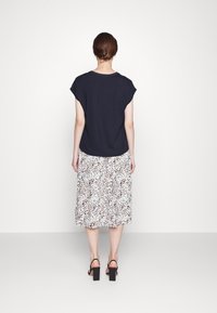 Haut marine à manches courtes, coupe décontractée, associé à une jupe blanche avec un subtil imprimé animal. Des sandales à talons blocs noires complètent le look.