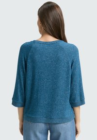 Blauer Strickpullover mit Dreiviertelärmeln, einem runden Halsausschnitt und einer lockeren Passform. Sichtbare strukturierte Oberfläche und gerippte Saumdetails.