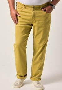 Žluté bavlněné kalhoty se střihovým rovný fit, designem pěti kapsiček a ohrnutými manžetami, spárované s bílými a šedými teniskami.