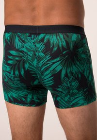 Slip boxer neri con motivo tropicale a foglie verdi, vita elastica e design aderente. Presentano una texture liscia e una lunghezza fino a metà coscia.