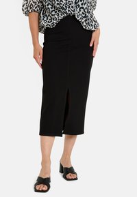 Jupe midi noire ajustée avec une fente à l'avant, faite d'un tissu lisse, associée à des sandales à talons blocs ouvertes noires.