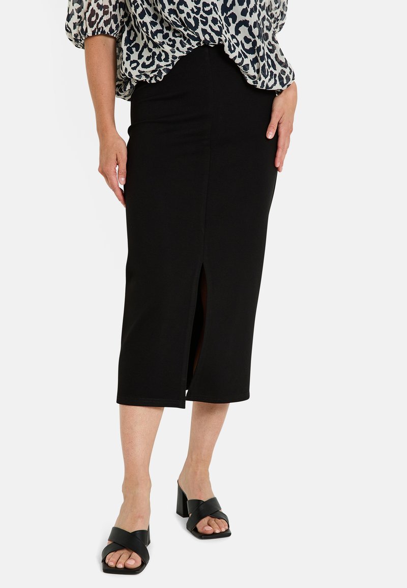 Jupe midi noire ajustée avec une fente à l'avant, faite d'un tissu lisse, associée à des sandales à talons blocs ouvertes noires.