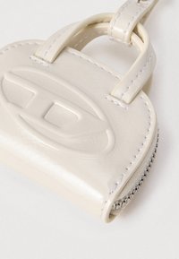 Geantă mică lucioasă din piele bej, cu siglă ovală embosată, margini cusute, fermoar și o curea cu buclă pe fundal alb.