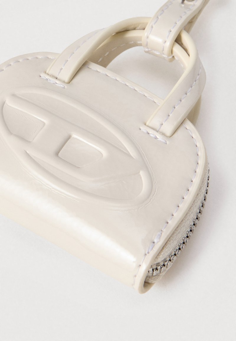 Kleine glänzende beige Lederetui mit ovalem, geprägtem Logo, genähten Kanten, Reißverschluss und einer Schlaufe auf weißem Hintergrund.