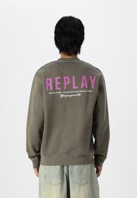 Sudadera gris con "REPLAY" en texto morado en negrita en la parte de atrás, con un corte relajado y puños acanalados. El texto a continuación detalla los servicios de la tienda de discos.