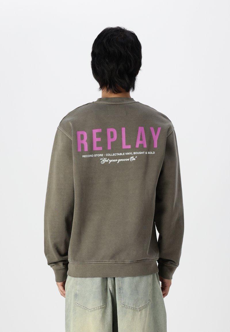 Grauer Pullover mit dem Aufdruck "REPLAY" in fettem lila Text auf der Rückseite, mit lockerem Schnitt und Rippbündchen. Text unten beschreibt die Dienstleistungen des Plattenladens.
