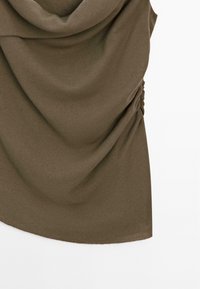 Olijfgroen stof met gerimpelde zijdetails en zachte draping op een witte achtergrond.