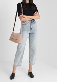 Světle růžová kabelka na rameno s hladkým povrchem, spárovaná s černým žebrovaným topem a světle modrými džíny s vysokým pasem, které mají zkrácený střih.