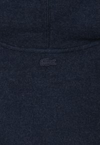 Tessuto di lana blu scuro con cuciture sottili e un dettaglio ricamato di un logo coccodrillo tonale.