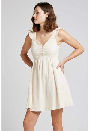 Robe crème claire avec des bretelles à volants, corsage ajusté et jupe loose froncée. Fabriquée en tissu texturé avec des motifs subtils.