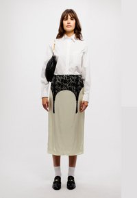 Cămașă albă cu mânecă lungă, fustă crem cu dantelă, geantă neagră, pantofi negri și șosete albe. Fusta are modele și accente distincte.