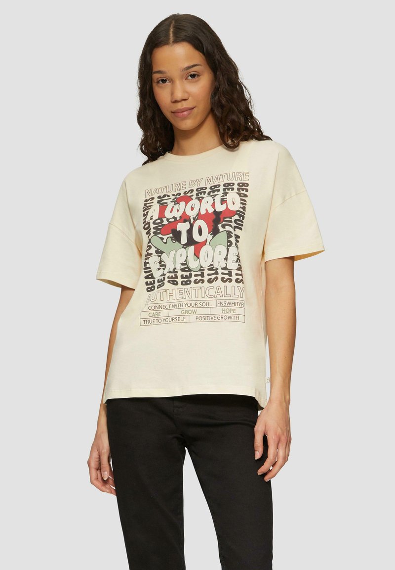 Crème-kleurig oversized t-shirt met een grafisch ontwerp van tekst en abstracte vormen in rood en groen. Korte mouwen en ronde halslijn.