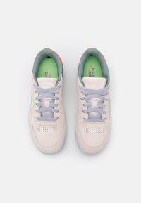 Ljusrosa sneakers med grå snören, gröna innersulor och röda accenter. Har perforerade detaljer på tån och en rundad form.