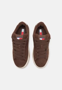 Brune semskesneakers har en teksturert finish med tykke, brune lisser. Innvendig har de en såle med logo med røde, hvite og blå detaljer.